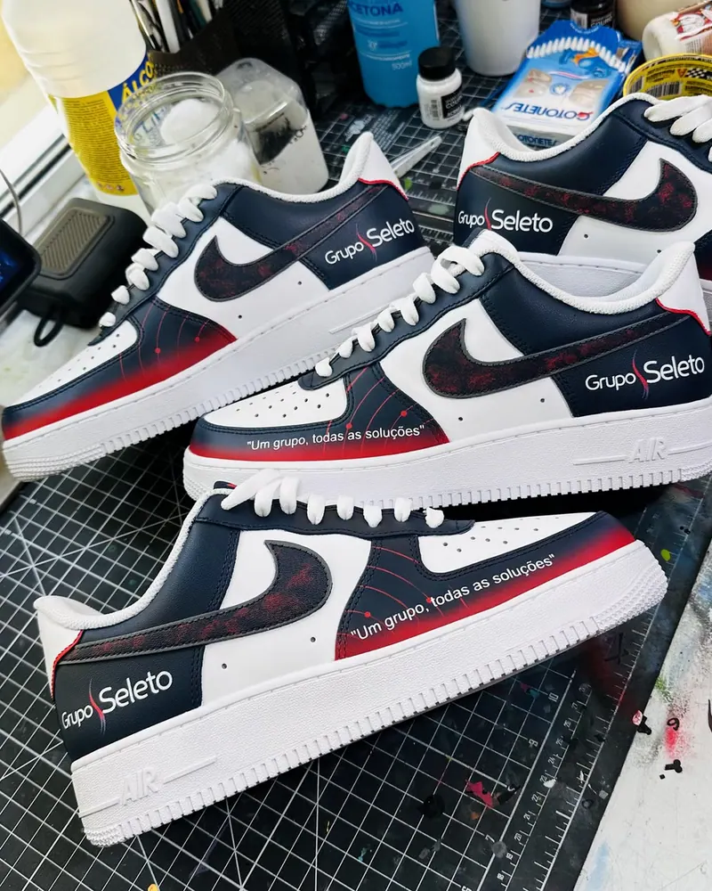 Tênis azul marinho e vermelho pintados à mão com a marca Grupo Seleto e a frase Um grupo, todas as soluções