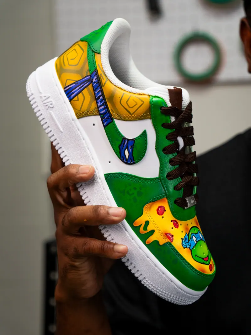 Tênis branco e verde pintado à mão com a Tartaruga Ninja de bandana azul sobre pizza
